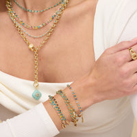 Close-up of a person wearing multiple necklaces, bracelets, and rings with turquoise and gold accents.
