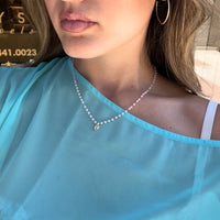 Woman wearing an aqua top with a white sprinkle solitaire necklace in front of the Lucky Star Jewels showroom.