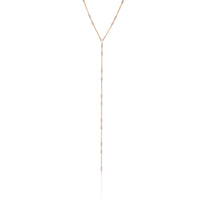 A gold lariat necklace with small metallic chain details and a silver accent, displayed against a white background.